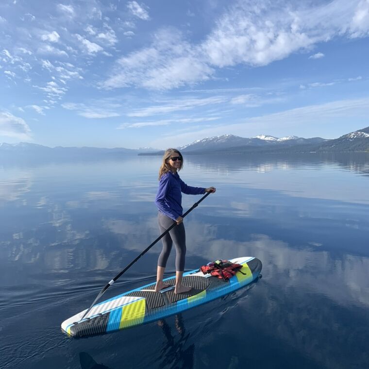 A paddleboarder crossing Lake Tahoe on a morning calm enough to mirror the clouds