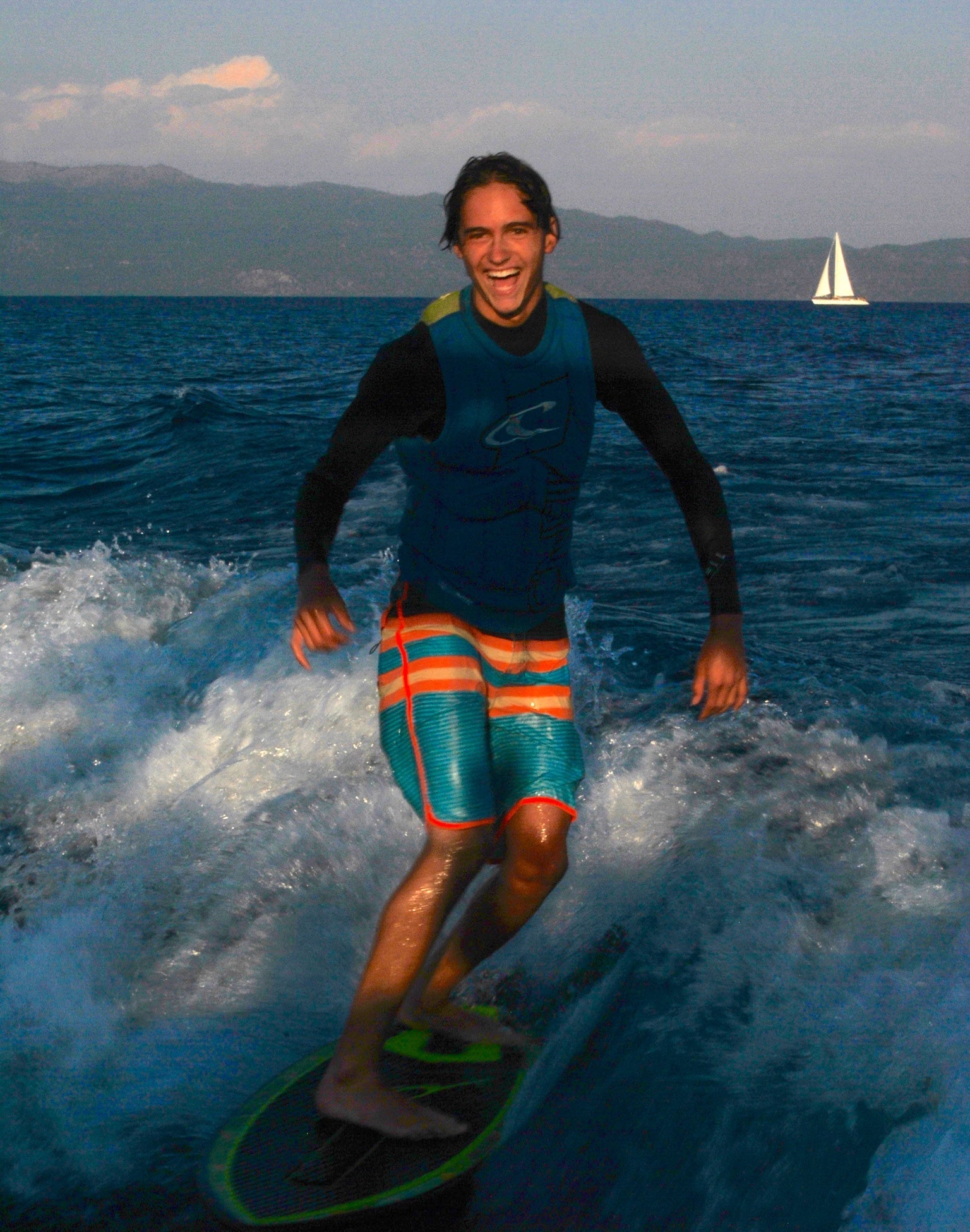 Person surfing on a wave with a sailboat in the distance