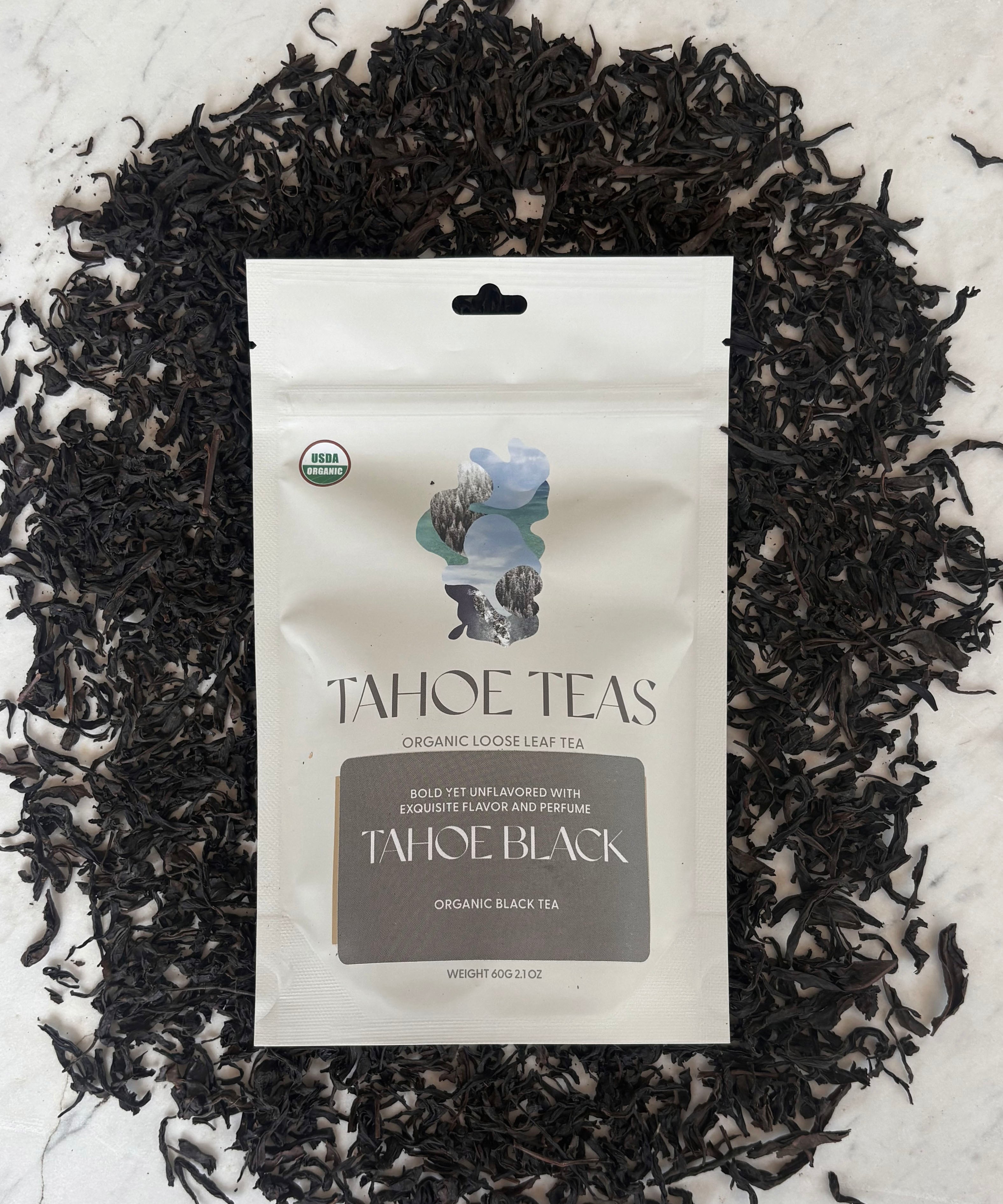 Tahoe Black tea package on marble, surrounded by loose black tea leaves