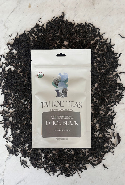 Tahoe Black tea package on marble, surrounded by loose black tea leaves