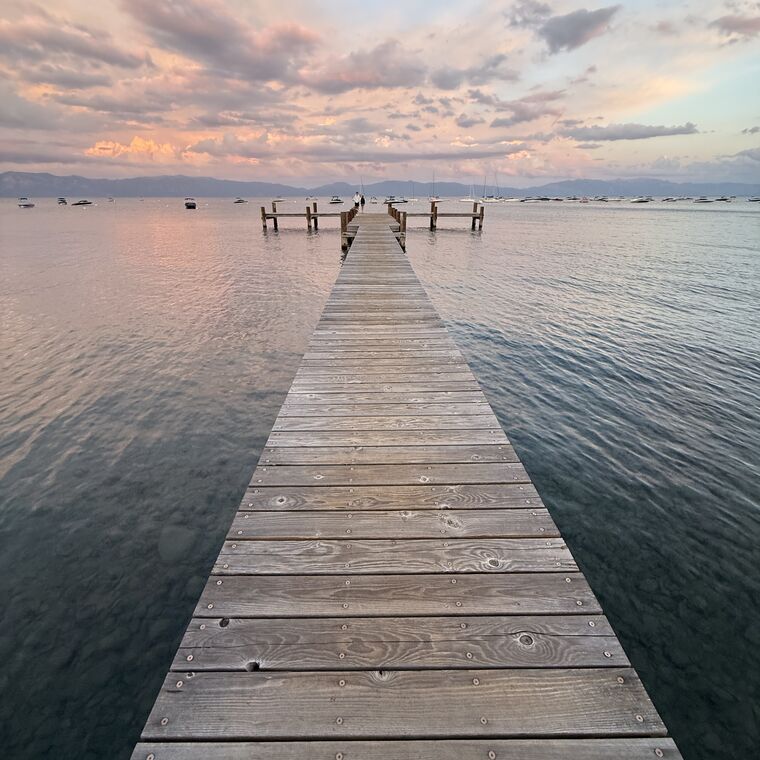 A wooden pier running out into flat water at first light