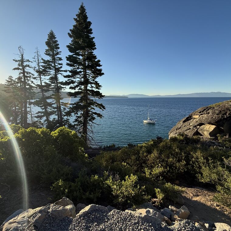A sailboat anchored in a turquoise cove below Jeffrey pines