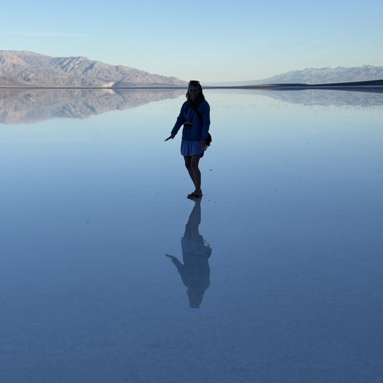 A woman standing on water so still it mirrors her and the mountains behind
