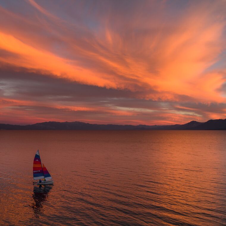 A small sailboat crossing Lake Tahoe under a sky burning orange at sunset