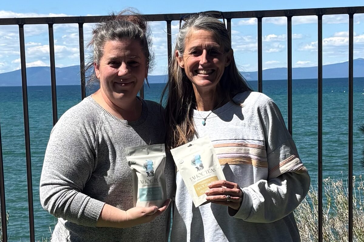 Two people holding Tahoe Teas pouches on a deck above Lake Tahoe